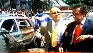 A la derecha el exministro Fernando Londoño con un guardaespalda y un carro destruido a la izquierda.